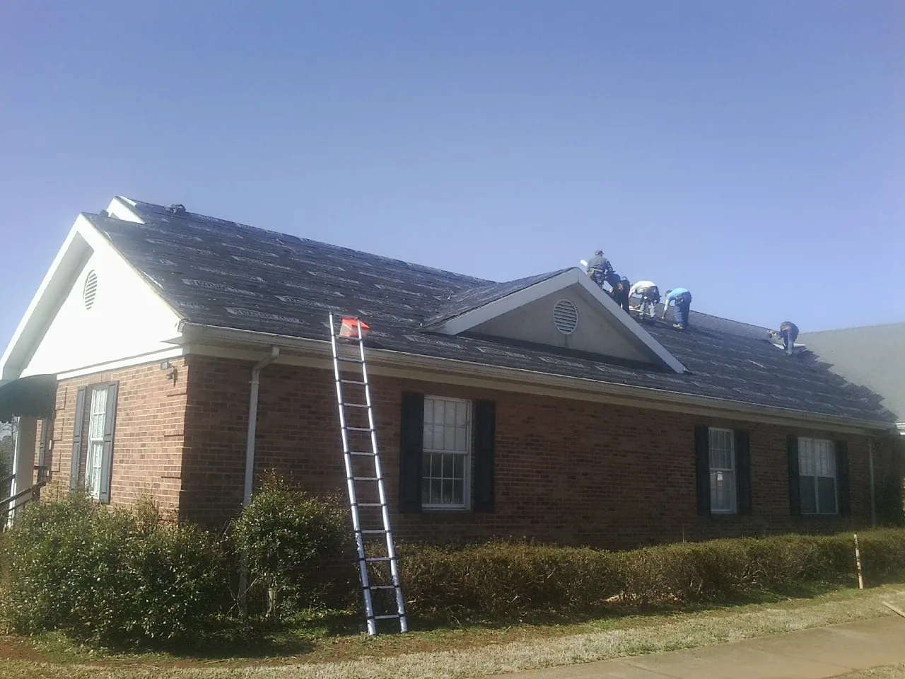 Crew tearing shingles off a brick ranch roof with a ladder set — Emergency Roof Repair work by our crew in Loch Sheldrake