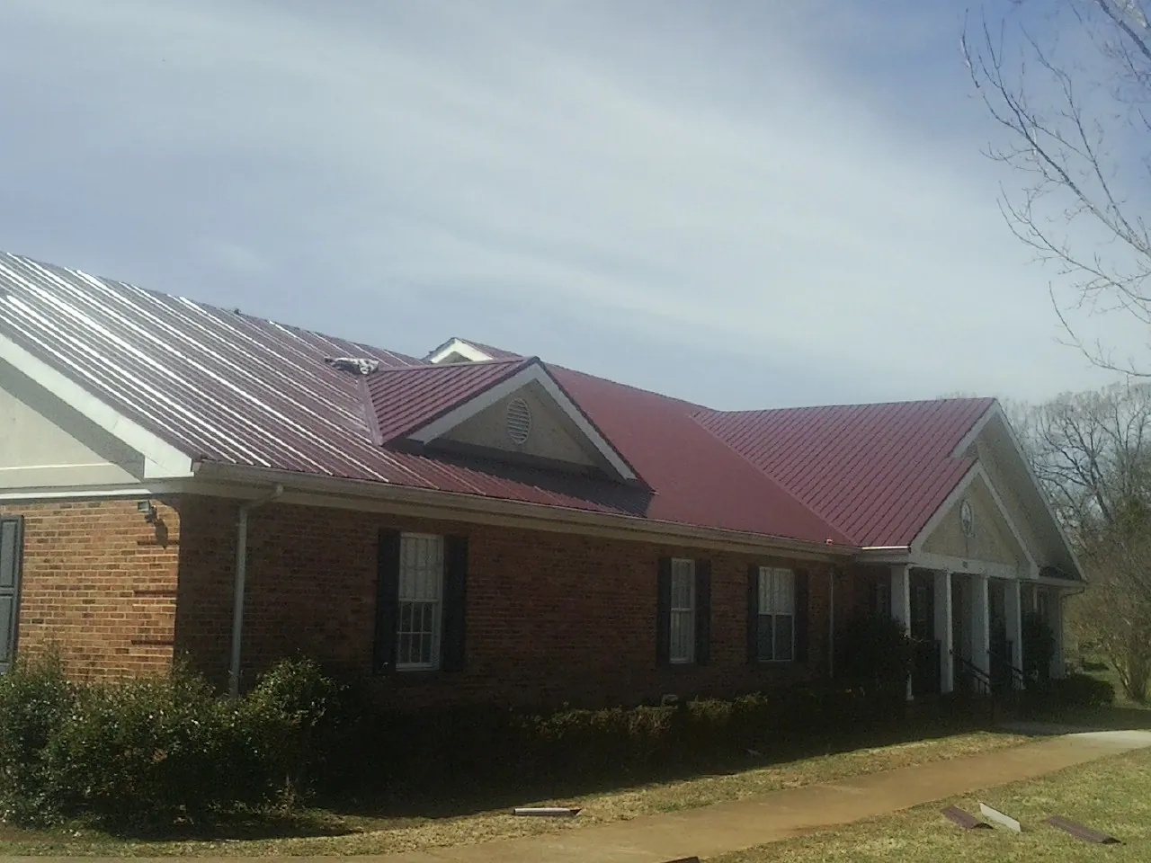 Red metal roof with gabled entries on a long brick building, from a Hail Damage Roof Repair job in Loch Sheldrake