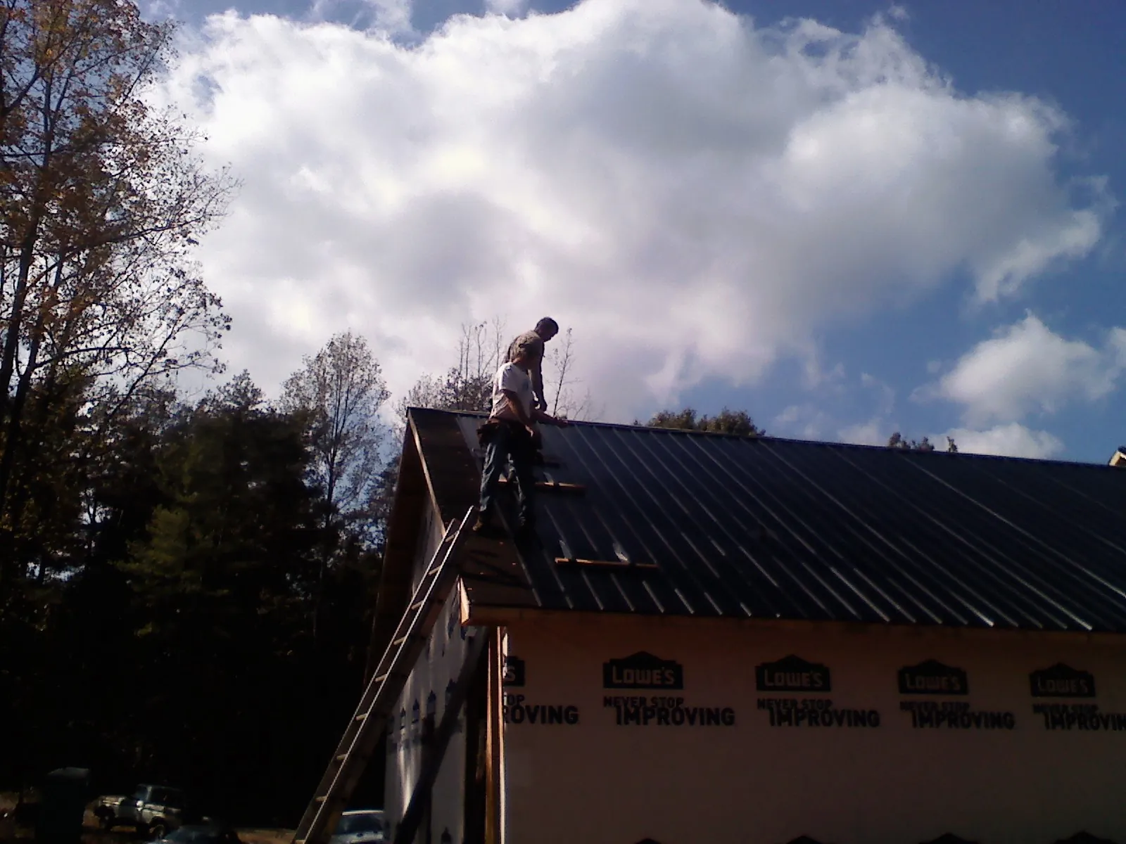 Roofer fastening dark metal panels high against a cloudy sky, from a Roof Inspection job in Loch Sheldrake
