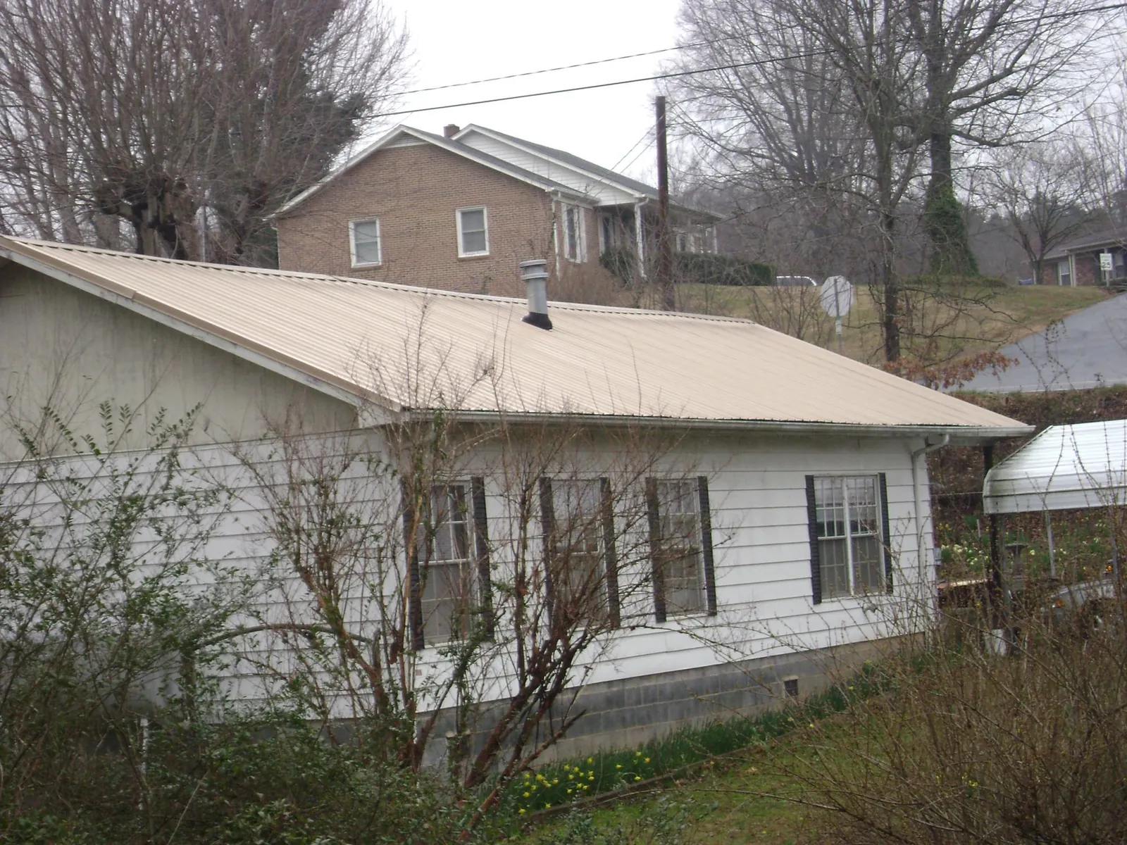 Tan metal roof on a white sided house set into a hillside — Commercial Roofing by Roofing Brothers in Loch Sheldrake