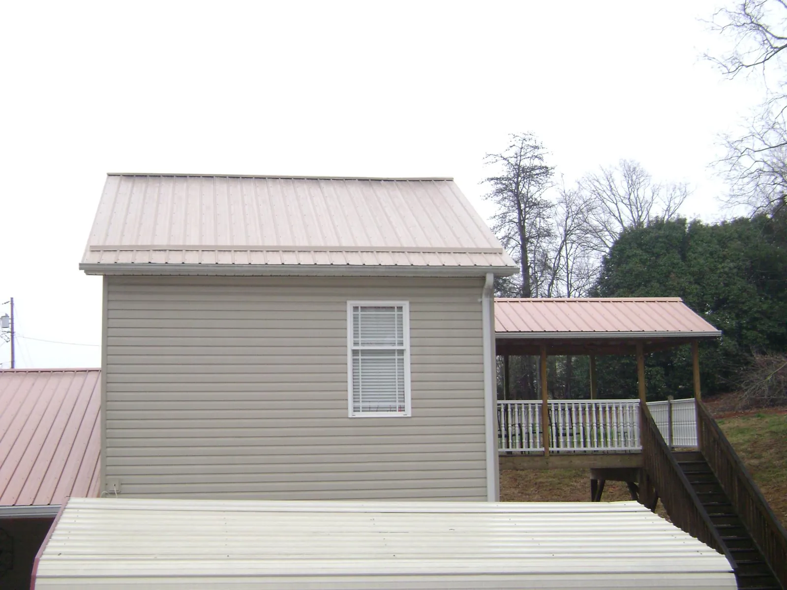 Tan metal roofs on a two story addition and attached porch, from a Roof Replacement job in Loch Sheldrake